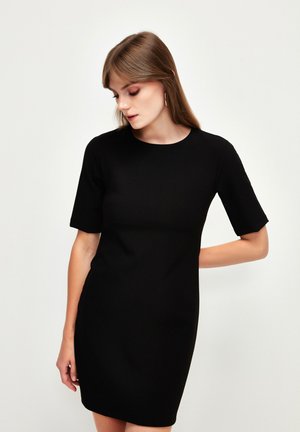 Abito nero a maniche corte con scollatura rotonda. Realizzato in un materiale liscio, ha una silhouette aderente e arriva sopra le ginocchia.