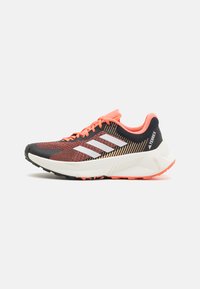 Zapatilla de running para hombre con parte superior de malla negra y marrón, con tres franjas blancas, detalles en naranja y una suela texturizada para tracción.