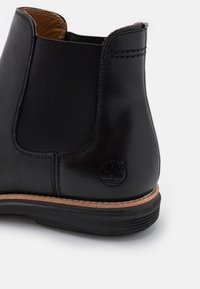 Bottine Chelsea en cuir noir avec panneaux latéraux élastiques, détails cousus et semelle en caoutchouc avec une semelle intermédiaire marron clair contrastante.