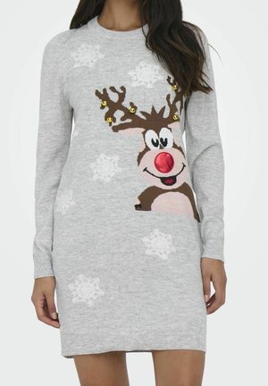 Femme portant une robe-pull grise avec un motif de renne souriant, un nez rouge, des grelots dorés sur les bois et des flocons de neige blancs.