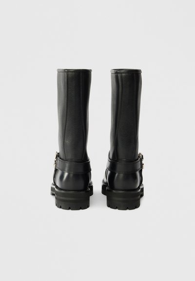 Μαύρες δερμάτινες μπότες μέχρι το γόνατο με στρογγυλή μύτη, υφή, ανθεκτική σόλα και λεπτομέρεια με λουρί που κλείνει με αγκράφα στον αστράγαλο.