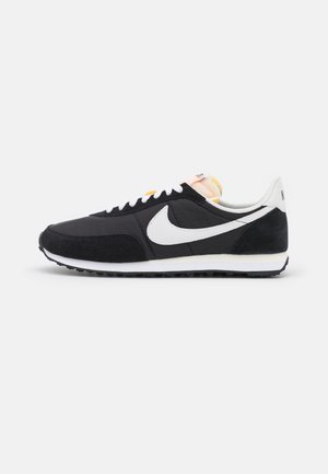 Baskets de sport noires en suede et en mesh, avec un swoosh Nike blanc, des accents jaunes et une semelle blanche contrastante.