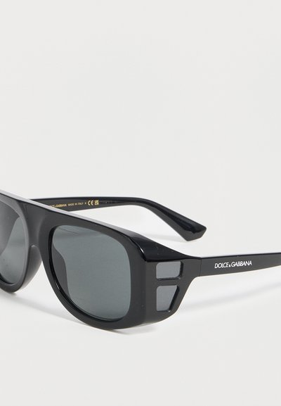Μαύρα ορθογώνια γυαλιά ηλίου Dolce & Gabbana με σκούρα φακούς και λογότυπο στο πλάι, εμφανίζονται σε απλό λευκό φόντο.