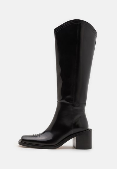 Black leather knee-high boot with a square toe, mid-block heel, and decorative stitching. Smooth, glossy finish with a structured design.