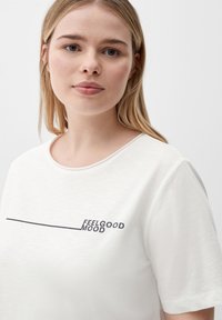 Bijela pamučna majica s okruglim izrezom, s crnim printom koji kaže "FEELGOOD MOOD" u modernom, minimalnom stilu.