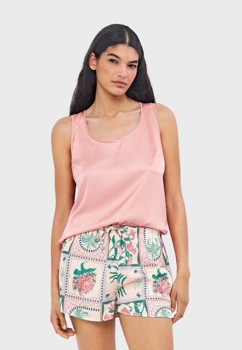 Femme aux longs cheveux foncés portant un haut sans manches rose pâle et un short à motifs floraux avec une taille à cordon.
