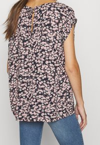 Bloemige blouse in donkerblauw met roze en witte bloemen, ronde hals met een keyhole-sluiting aan de achterkant, en korte mouwen.