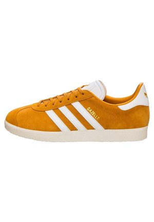 Oranje suède Adidas Gazelle sneaker met witte strepen, witte hielcap en beige rubberen zool gezien van opzij.