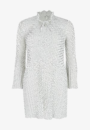 Robe blanche à pois noirs, avec des manches longues, un col volanté et un corsage ajusté qui s'évasent à la taille.