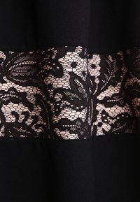 Svart tyg med ett horisontellt band av intrikat svart blommig spets över en ljusbeige bakgrund.