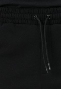 Schwarze Jogginghosen mit elastischem Bund, ausgestattet mit einem Kordelzug mit schwarzen Verstellern und einer glatten, matten Stoffstruktur.