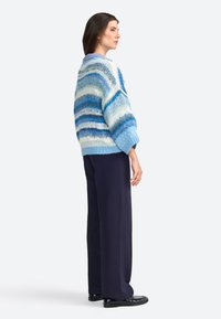 Suéter de punto de gran tamaño a rayas azules y blancas con un acabado texturizado, combinado con pantalones de pierna ancha en navy y zapatos negros.