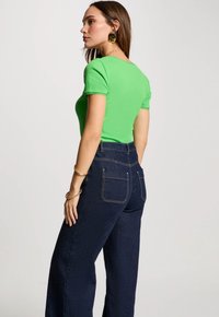 Groen geribbeld T-shirt met gegolfde mouwen, gecombineerd met donkerblauwe high-waisted jeans met achterzakken en lichte stikdetails.