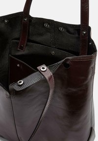 Brązowa skórzana torba typu tote o gładkiej fakturze, z metalowymi detalami i dwiema mocnymi uchwytami. Wnętrze zawiera wiele przegród.