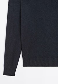 Maglione lavorato a maglia di un blu scuro, con collo rotondo, polsini e orlo a coste, e una texture morbida. Il design è a maniche lunghe con dettagli minimi.