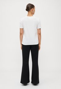 T-shirt blanc à manches courtes avec un col rond, associé à un pantalon noir évasé, vu de dos, mettant en valeur une texture lisse.