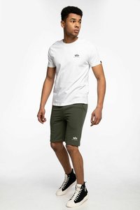 T-shirt en coton blanc avec un petit motif sur la poitrine, associé à un short vert olive avec des poches latérales et un logo au niveau de l'ourlet. Baskets montantes noires.