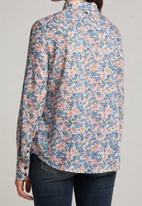 Camicia a maniche lunghe floreale con un vivace motivo di fiori blu e pesco su uno sfondo chiaro, tessuto morbido e polsini abbottonati.