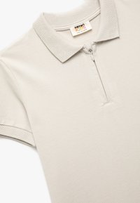 Camisa polo gris claro con cuello con cremallera, cuello acanalado y acentos texturizados en las mangas. Fabricada con una tela suave y transpirable.