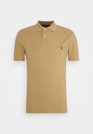 Beige polo tričko vyrobené z bavlny s dvoutlačítkovou légou, ribbeným límečkem a malým vyšívaným logem na levé hrudi. Krátké rukávy.