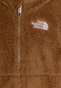 Brązowa kurtka z polaru na suwak o teksturowanej powierzchni, z haftowanym logo po lewej stronie na piersi i suwakiem z przodu.