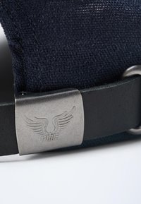 Gorra de tela navy con acabado texturizado, que presenta un cierre metálico plateado y un detalle del logotipo de ala grabado en una correa de cuero oscuro.