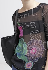 Blouse noire transparente avec des motifs floraux colorés en vert, rose et violet. Accompagnée d'un sac à épaule en cuir noir.