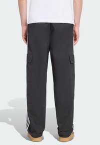 Svarta cargobyxor i lättviktstyg med två sidfickor och vita randdetaljer längs nedre benen, kombinerade med beige skor.