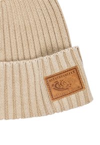 Bonnet en tricot beige avec une texture côtelée, comportant un patch en cuir marron rectangulaire portant l'inscription "élément depuis 1992" sur le revers.