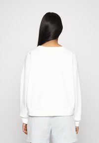 Sweatshirt blanc à col rond avec une coupe décontractée, des épaules tombantes et des poignets côtelés. Texture lisse, design décontracté, uni sans motifs.