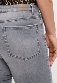 Gray denim jeans with two back pockets, subtle stitching details, and a branded leather patch at the waistband.