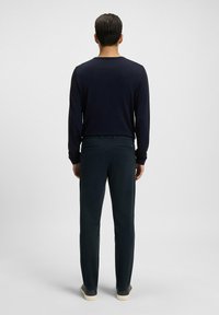 Navy long-sleeve shirt paired with dark green pants. Ribbed neckline, smooth texture, and visible back pockets. Casual footwear completes the outfit.
