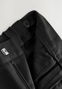 Schwarze Stoffhosen mit Reißverschluss, ausgestattet mit einem glatten Innenfutter, mehreren Taschen und einem Markenetikett am Bund.