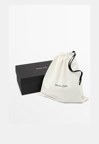 Sac en coton avec cordon de serrage en crème, portant "Massimo Dutti" imprimé en noir. Une boîte noire rectangulaire est partiellement visible en dessous.