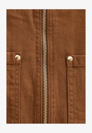 Zbliżenie na brązową lnianą kurtkę z centralnym metalowym zamkiem błyskawicznym i dwoma przednimi kieszeniami zabezpieczonymi metalowymi zatrzaskami.