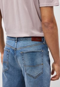 Ανοιχτού μπλε τζιν παντελόνια με δύο πίσω τσέπες, ορατές ραφές και καφέ δερμάτινη ετικέτα με το λογότυπο "Pepe Jeans" στη μέση.