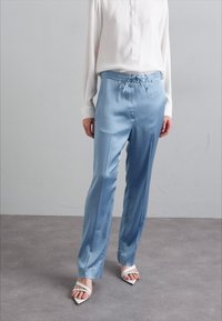 Light blue satin pants with an elastic waistband and drawstring, featuring a straight-leg fit and paired with a white blouse and sandals.