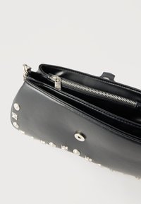 Μαύρο δερμάτινο τσαντάκι χειρός με ασημένιες τρουκ, ανοιχτό πάνω μέρος που αποκαλύπτει εσωτερικό φερμουάρ και κούμπωμα με κουμπί πάτημα.