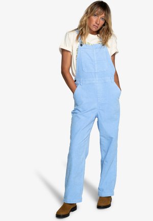Light blue corduroy overalls with a loose fit, featuring adjustable straps and front pockets, paired with a white t-shirt and brown boots.