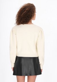 Elefántcsont színű kötött pulóver puffos ujjakkal és kerek nyakkivágással, rövid fekete bőrszoknyával párosítva, hátulról nézve.