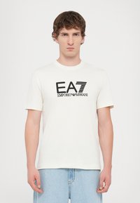 White cotton t-shirt featuring a black EA7 Emporio Armani logo, crew neck, and short sleeves; smooth texture with no patterns or accents.