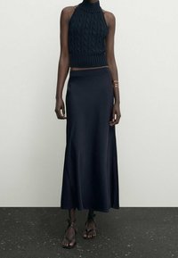 Haut court en tricot navy à col halter avec un motif en cable associé à une jupe lisse de longueur genoux. Des sandales à fines brides complètent l'ensemble.