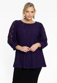 Paarse kantblouse met driekwart pofmouwen, ontworpen met getextureerde bloemenpatronen, gecombineerd met een zwarte rok.