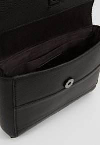 Černá kožená psaníčko s otevřeným klopou, která odhaluje látkovou podšívku uvnitř a stříbrné magnetické zapínání na přední straně.