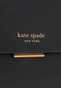 Black leather handbag featuring gold-tone logo "kate spade NEW YORK" and a gold accent hardware piece. Textured surface with a sleek design.