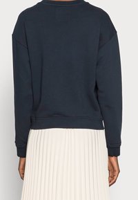 Marinblå sweatshirt i mjukt tyg med rundad halsringning, sänkta axlar och ribbade muddar, kombinerad med en veckad krämfärgad kjol.