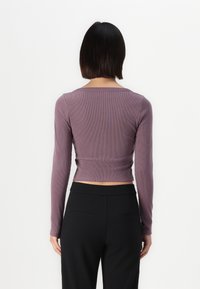 Ilga rankovė, trumpa mauve spalvos viršutinė dalis su spraginiu dekoltė, su raukšlėta tekstūra. Derinama su juodomis aukšto liemens kelnėmis, turinčiomis nugaros kišenių detales.