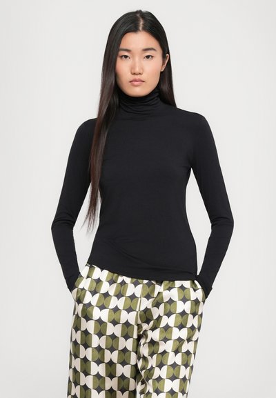 Zwarte lange mouwen coltrui gemaakt van een gladde, rekbare stof, gecombineerd met gestreepte wijde broek met groene en crème cirkels.