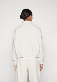 Light beige fleece pullover with high collar, elastic waistband, and cuffs. Features a relaxed fit and soft texture. Viewed from the back.