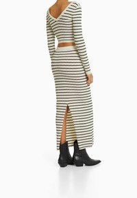 Stickad tvådelad set med en figurnära långärmad topp och en lång kjol. Färgen är krämvit med svarta horisontella ränder och sidöppning. Bärs med svarta stövlar.